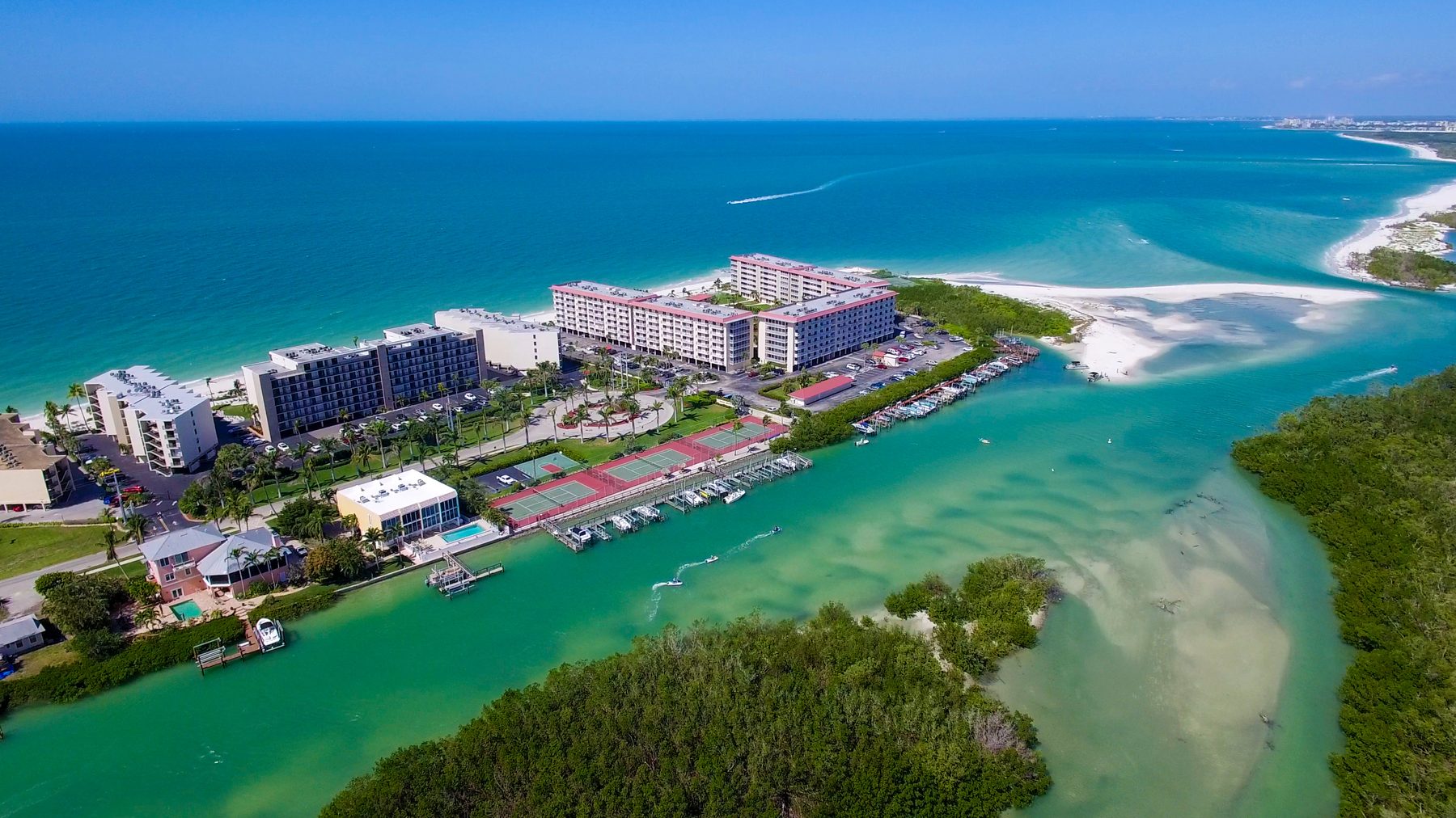 Aerial view of a barrier island community with condos, marina, and Gulf beach